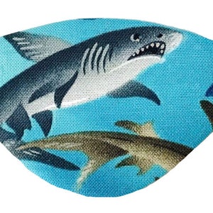 May include: A blue eye patch with a shark pattern. The patch features a large shark with white teeth and smaller sharks in the background.