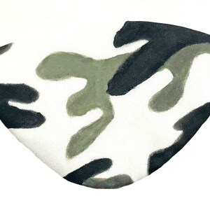 May include: A white eye patch with a camouflage pattern in black and green. The eye patch has an elastic band.