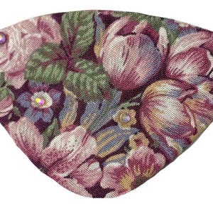 May include: An eye patch with a floral design, featuring pink and purple flowers and green leaves. The patch has a black elastic strap and small, iridescent gems.