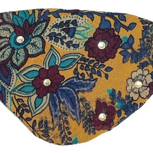 May include: A yellow fabric eye patch with a paisley pattern in shades of blue, teal, and burgundy. The patch has gold-colored studs around the edges.