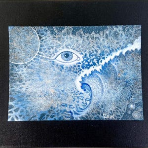 Op de afbeelding: Abstract schilderij op canvas, met een groot blauw oog, een halve maan en een gezicht. Het kunstwerk is overwegend blauw en wit, met een zwarte lijst. De handtekening van de kunstenaar, "LAIN", is rechtsonder zichtbaar.