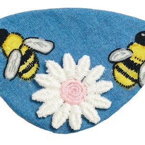 May include: A blue denim eye patch with embroidered bees and a white daisy with a pink centre.