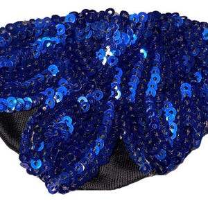 May include: A blue sequined eye patch with a black backing and elasticated band. The sequins are a vibrant blue and cover the front of the patch. The eye patch is designed to cover one eye.
