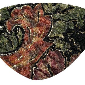 May include: A black fabric eye patch with a floral pattern in shades of gold, red, and green. The fabric is textured and appears to be beaded.