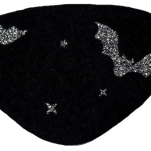 May include: A black eye patch featuring two silver glitter bat silhouettes and three small silver glitter star shapes. The eye patch is constructed from a solid black fabric and includes a thin black elastic strap attached to each side for secure placement.