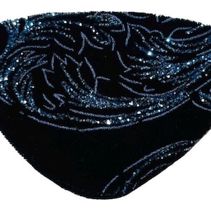 May include: Black eye patch with a velvet texture and an intricate, swirling design. The design is embellished with sparkling blue sequins. The eye patch has an elastic band for secure wear.