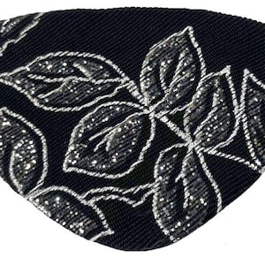 Pode incluir: Um tapa-olho com base de tecido preto e um padrão de folhas bordadas em prata. O design consiste em várias folhas com costuras prateadas detalhadas sobre o fundo escuro. Uma fina tira elástica preta está fixada na lateral.