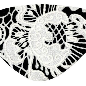 May include: An eye patch featuring a black base fabric overlaid with a white lace pattern. The lace design consists of intricate floral and swirling motifs. The patch is shaped to cover one eye and includes a thin black elastic strap on each side.