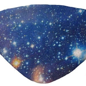 May include: A fabric eye patch with a blue galaxy print, featuring white and yellow stars. Two small, blue rhinestones are placed on the patch. A black elastic band is attached for wear.