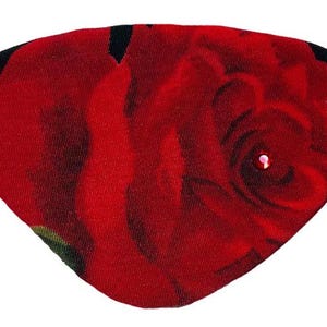 Puede incluir: Una máscara para los ojos de tela con una rosa roja sobre un fondo negro y un strass en el centro.