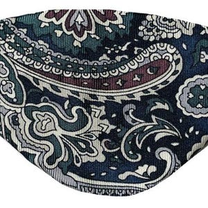 Könnte beinhalten: Eine Gesichtsmaske mit Paisley-Muster in den Farbtönen Marineblau, Türkis, Burgunderrot und Grau. Die Maske hat auf jeder Seite ein Gummiband für sicheren Halt. Das Design umfasst komplizierte Blumen- und Tropfenmotive.