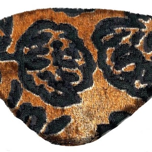 Könnte beinhalten: Eine braun-schwarze Augenmaske mit Gummiband. Die Maske hat ein Blumenmuster aus schwarzem Samt auf braunem Grund. Die Augenmaske ist so konzipiert, dass sie das Licht blockiert.