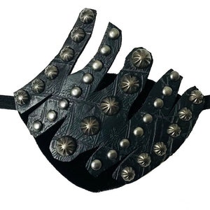 Puede incluir: Un parche para el ojo de cuero negro con tachuelas plateadas. El parche tiene una superficie texturizada y se asegura con una correa elástica.