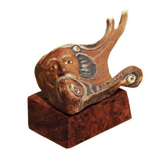 May include: A wooden sculpture of a bearded man's face with blue and white painted details. The sculpture is mounted on a dark wood base.