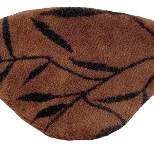 May include: Brown eye patch with a leaf design in black. The eye patch is made of a soft, textured material and has a black elastic band. The leaf pattern covers the entire surface of the eye patch.