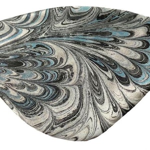 May include: A marbled eye patch with a black elastic band. The fabric features a swirling pattern in shades of gray, black, and teal. The eye patch is designed to cover one eye and is likely used for medical or fashion purposes.