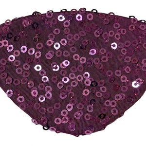 May include: A purple sequined eye patch with a black elastic strap. The fan-shaped eye patch is covered in small, shiny, round sequins. The sequins are a lighter shade of purple than the fabric.