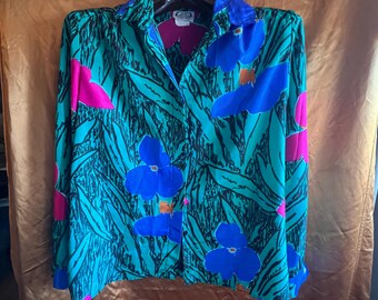 Könnte beinhalten: Ein langärmliges Button-Down-Hemd mit einem lebendigen Blumenmuster. Das Hemd hat große blaue und rosa Blüten vor einem türkisfarbenen Hintergrund mit schwarzen blattartigen Details. Der Kragen und die Manschetten sind einfarbig blau.