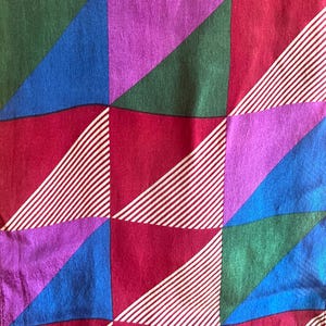 Peut inclure: Gros plan sur un tissu à motif géométrique. Le motif présente des carrés divisés en triangles dans des tons de rouge, vert, bleu et violet. Des rayures diagonales blanches ajoutent du contraste au design coloré.