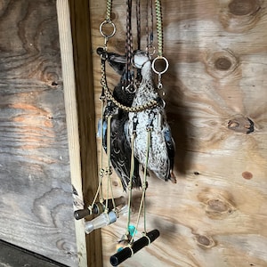 Puede incluir: Un accesorio de caza con dos señuelos de pato colgados de una estructura de madera. Los señuelos están suspendidos por cuerdas trenzadas, con reclamos de pato adjuntos. El fondo es una pared de madera.