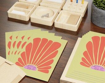 May include: A stack of rectangular cards featuring a light yellow background with a coral-colored fan-shaped graphic and a textured purple semi-circle base. The cards are displayed alongside a light-colored wooden desk organizer set.
