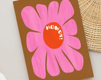 May include: A rectangular greeting card with a brown background featuring a large, stylized pink flower with long, rounded petals. The center of the flower is a solid orange circle with the white text "HOWDY!" printed in a bold, rounded font.