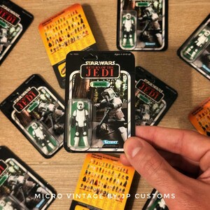 Może przedstawiać: Opakowanie po figurce akcji Star Wars w stylu vintage z Scout Trooper z Return of the Jedi. Figurka znajduje się w przezroczystym plastikowym etui, z czarno-białym zdjęciem postaci na karcie. Opakowanie jest od Kenner.