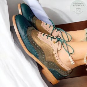Op de afbeelding: Tweekleurige leren brogues in teal, olijfgroen, beige en roze. De schoenen hebben decoratieve perforaties en lichtbruine zolen. De veters zijn teal.