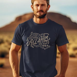 May include: A navy blue short-sleeve t-shirt featuring a beige graphic print on the chest. The design includes the text "LIVE THE VERSE" above the word "ALL4HIM" and "EST. 1994" with decorative swirling lines surrounding the lettering.