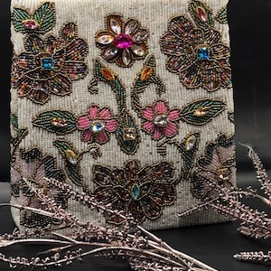 May include: Ivory beaded handbag with floral embroidery. The bag features colorful beaded flowers with pink, purple, and blue accents. The bag has a gold chain strap and is decorated with gemstones.
