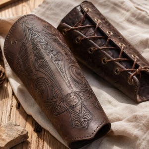 May include: A pair of dark brown leather bracers featuring intricate embossed patterns, including a central sword-like motif, swirling designs, and runic symbols. The bracers are secured with thin brown leather laces threaded through metal eyelets.