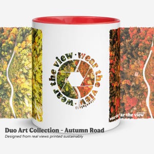 Op de afbeelding: Witte keramische mok met een rode binnenkant, met een ontwerp van een herfstweg. De mok heeft de tekst "wear the view" en "Duo Art Collection - Autumn Road" erop gedrukt. Het ontwerp is duurzaam gedrukt.