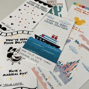 May include: A collection of whimsical greeting cards with various designs, including a cruise ship, a castle, and Mickey Mouse. The cards feature phrases like "You've Been Pixie Dusted!" and "Have a Magical Day!" with space for personalization.
