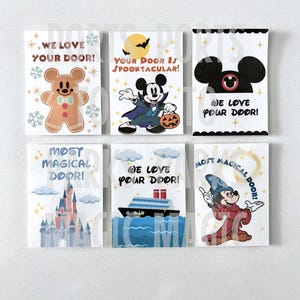 Puede incluir: Seis tarjetas rectangulares con varios diseños y texto. Las tarjetas presentan ilustraciones de un hombre de jengibre, Mickey Mouse con disfraz de vampiro, orejas de Mickey Mouse, un castillo, un crucero y Mickey Mouse como mago. El texto incluye "WE LOVE YOUR DOOR!" y "MOST MAGICAL DOOR!"