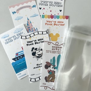 May include: A selection of colourful "You've Been Pixie Dusted" cards featuring designs such as a cruise ship, Mickey Mouse, a castle, and a cowboy Mickey. The cards are presented in a clear plastic bag.