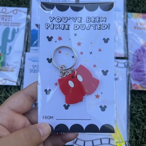 May include: A red Mickey Mouse-shaped keychain with white accents, attached to a silver keyring. The keychain is packaged in a clear plastic bag with a card that reads "YOU'VE BEEN PIXIE DUSTED!" and has Mickey Mouse silhouettes.