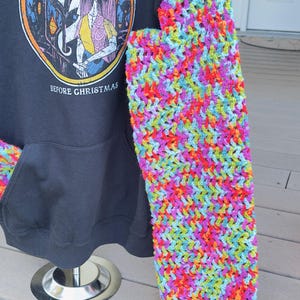 Puede incluir: Sudadera con capucha negra con una manga y un cord&oacute;n de ganchillo de colores. La sudadera presenta un gr&aacute;fico de "Pesadilla antes de Navidad". La manga de ganchillo est&aacute; hecha de hilo de arco&iacute;ris.