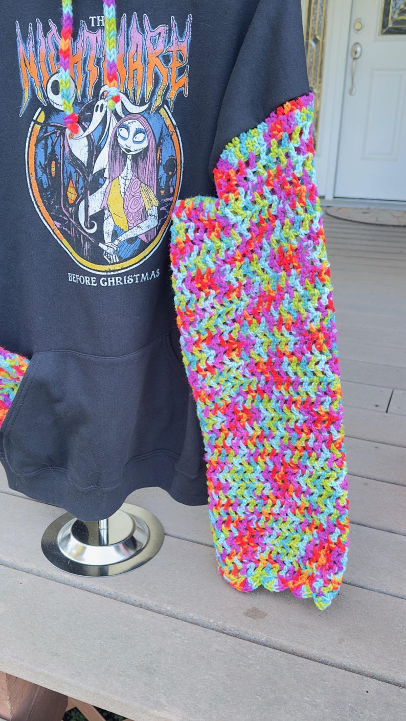 Puede incluir: Sudadera con capucha negra con una manga y un cord&oacute;n de ganchillo de colores. La sudadera presenta un gr&aacute;fico de "Pesadilla antes de Navidad". La manga de ganchillo est&aacute; hecha de hilo de arco&iacute;ris.