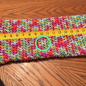 Puede incluir: Una manga de ganchillo colorida con un patr&oacute;n vibrante de rosa, azul, amarillo y verde. Una regla amarilla muestra que la manga mide aproximadamente 53 cm de largo. La manga est&aacute; unida a una prenda negra.