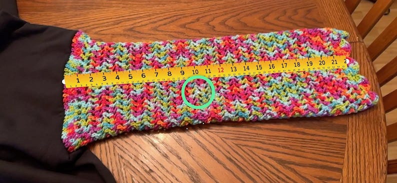 Puede incluir: Una manga de ganchillo colorida con un patr&oacute;n vibrante de rosa, azul, amarillo y verde. Una regla amarilla muestra que la manga mide aproximadamente 53 cm de largo. La manga est&aacute; unida a una prenda negra.