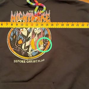 Puede incluir: Sudadera con capucha negra con mangas de ganchillo coloridas. La parte delantera presenta un gr&aacute;fico de "Pesadilla antes de Navidad". Las mangas miden aproximadamente 56 cm de largo. El cord&oacute;n de la capucha es arco&iacute;ris.