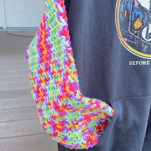 Puede incluir: Una sudadera con capucha negra con una manga y un bolsillo de ganchillo coloridos. La manga est&aacute; hecha de hilo vibrante en tonos de rojo, naranja, amarillo, verde, azul y morado. La sudadera tiene un gr&aacute;fico en la parte delantera.