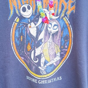 Puede incluir: Sudadera con capucha azul marino con un dise&ntilde;o gr&aacute;fico de "Pesadilla antes de Navidad". El dise&ntilde;o incluye a Jack Skellington y Sally, con el texto "The Nightmare Before Christmas". La capucha tiene un cord&oacute;n arco&iacute;ris.