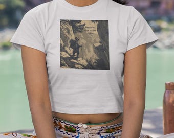 Könnte beinhalten: Weißes Crop-Top mit einem Schwarz-Weiß-Bild einer Person, die einen Berg erklimmt. Die Person sitzt auf einer grünen Yogamatte mit gekreuzten Beinen. Beige Hose mit farbiger Stickerei.
