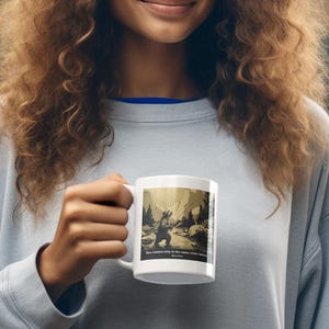 Puede incluir: Taza de cerámica blanca con una ilustración en tonos sepia de una persona en un bosque. La taza tiene el texto "No se puede entrar dos veces en el mismo río". La persona lleva una sudadera azul claro y un sombrero marrón.