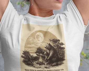 Könnte beinhalten: Weißes T-Shirt mit einer sepiafarbenen Illustration eines Bären und eines Jungen unter einem Vollmond. Der Text "Very little is needed to make a happy life" ist darunter gedruckt. Die Person trägt das T-Shirt mit erhobenen Armen.