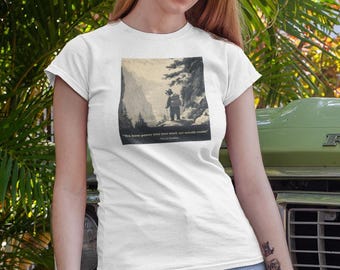 Könnte beinhalten: Weißes T-Shirt mit einem kleinen, gerahmten Schwarz-Weiß-Bild einer Person, die in einem Wald spaziert. Das Shirt wird mit einer blauen Jeans kombiniert. Ein braun-weißer Hund sitzt auf dem Gras neben einem grünen Oldtimer-Truck.