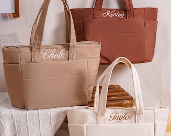 Puede incluir: Tres bolsos tote acolchados en colores beige, marrón y crema. Cada bolso cuenta con dos asas superiores, bolsillos laterales y un patrón de costuras horizontales. Los bolsos están personalizados con nombres bordados: Chole en el beige, Kesley en el marrón y Taylor en el crema.