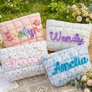 Può includere: Quattro pochette trapuntate in colori pastello, ciascuna ricamata con un nome: Evelyn, Wendy, Grace e Amelia. Le pochette sono su una superficie di legno con fiori e un invito di nozze. Le pochette hanno un motivo quadrato.