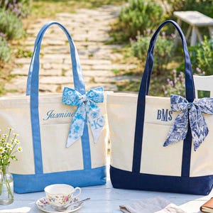 Puede incluir: Dos bolsos de mano de lona con detalles azules. Uno tiene el nombre "Jasmine" y una inicial "K", el otro "BMS". Ambos bolsos tienen un lazo azul a juego.